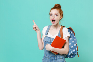 Shocked young readhead student girl in casual denim clothes with backpack isolated on blue...