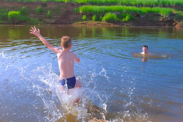 Dad and son, family, are swimming together in river at Summer warm day. Outdoors summer activity. Man and boy are bathing in river in wild place. Fatherhood, man playing with child, kid on nature.
