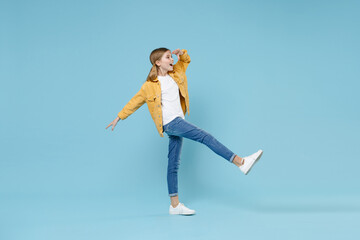 Full length portrait of amazed little blonde kid girl 12-13 years old in yellow jacket isolated on blue background. Childhood lifestyle concept. Holding hand at forehead looking far away distance.