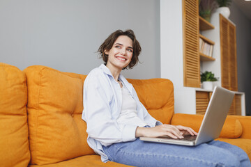 Smiling young woman girl in casual clothes sitting on couch spending time in living room at home....