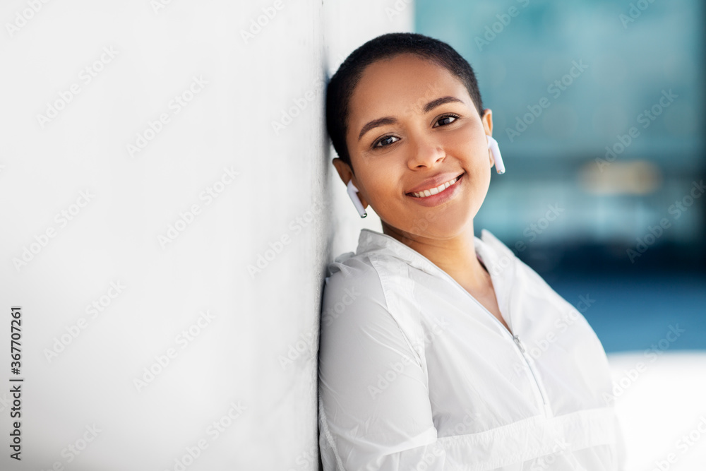 Wall mural fitness, sport and technology concept - happy smiling young african american woman with wireless ear