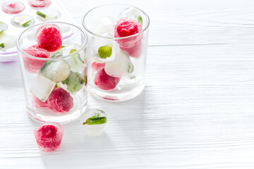 Cocktail glasses with berries in ice cubes on white table copy space