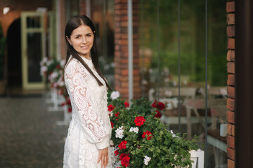 Portrait of beautiful woman in white dress outdoors. Attractive brunette in front of cafe