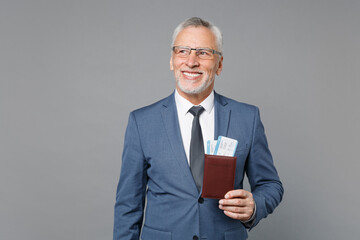 Smiling elderly gray-haired business man in classic blue suit shirt tie isolated on grey wall background. Achievement career wealth business concept. Hold passport ticket boarding pass, looking aside.