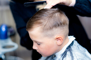 Close up caucasian american pretty school boy trendy haircut at bright modern barbershop.