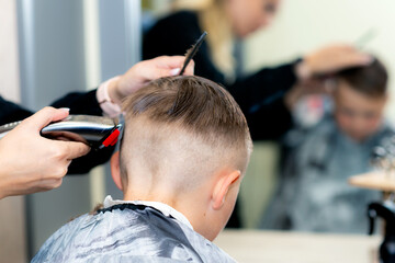 Back view Close up caucasian pretty school boy trendy haircut at bright modern barbershop.