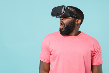 Amazed young african american man guy in casual pink t-shirt isolated on pastel blue background studio portrait. People lifestyle concept. Mock up copy space. Watching in headset, keeping mouth open.