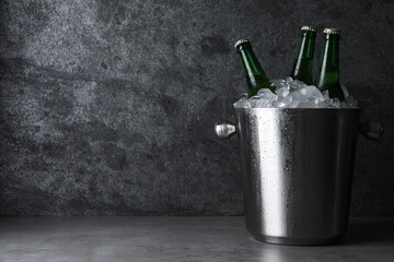 Metal bucket with beer and ice cubes on grey table. Space for text
