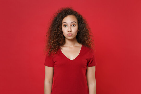 Pretty young african american woman girl in casual t-shirt posing isolated on red background studio portrait. People emotions lifestyle concept. Mock up copy space. Blowing lips, making duck face.