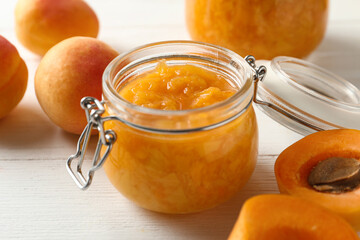 Jar of apricot jam and fresh fruits on white wooden table, closeup