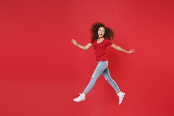 Fototapeta na wymiar Full length portrait side view of funny young african american girl in casual t-shirt isolated on red background studio. People lifestyle concept. Mock up copy space. Jumping spreading hands and legs.