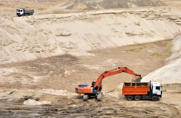 Excavator load the sand to the heavy dump truck in the open-pit. Heavy machinery working in the mining quarry. Digging and excavation operations. View on the mountains with yellow sand. Soft focus