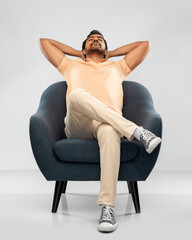 people and furniture concept - happy smiling young indian man sitting in chair over grey background