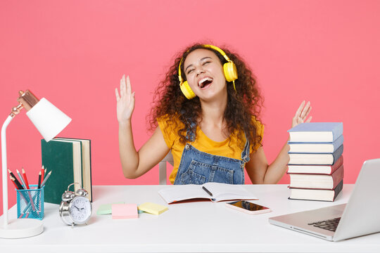 Happy african american girl employee in office sit work isolated on pink background. Achievement business career. Education in school university college concept. Listen music with headphones, dancing.