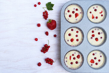 Summer baking - delicious homemade muffins with red berries - strawberries, raspberries and red currant. Baking tray with paper moulds filled with muffin dough, ready for baking. Fresh fruits around