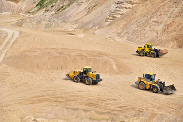 Wheel front-end loaders working at the sand open pit. Quarry in which sand and gravel is excavated from the ground. Mining industry