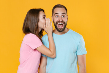 Surprised young couple friends guy girl in blue pink t-shirts isolated on yellow background studio...