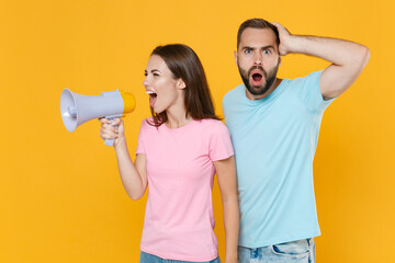 Shocked young couple two friends guy girl in blue pink t-shirts posing isolated on yellow wall...
