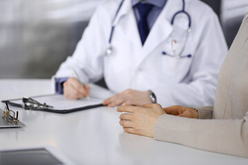 Unknown male doctor and patient woman discussing something while sitting in clinic and using clipboard. Best medical service in hospital, medicine, pandemic stop