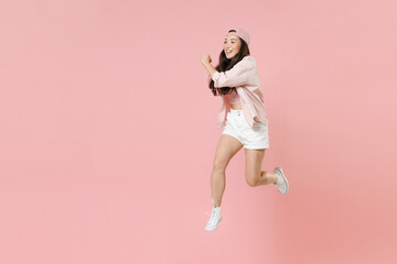 Full length portrait of cheerful young asian girl in casual clothes, cap isolated on pastel pink...