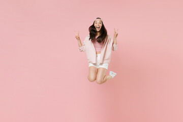 Full length portrait of cheerful young asian girl in casual clothes, cap isolated on pastel pink background studio portrait. People lifestyle concept. Mock up copy space. Jumping showing victory sign.