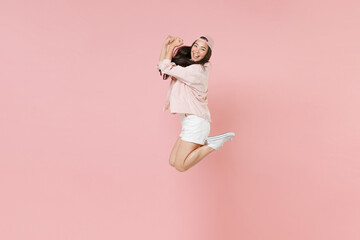 Full length portrait side view of happy young asian girl in casual clothes, cap isolated on pastel pink background studio. People lifestyle concept. Mock up copy space. Jumping doing winner gesture.
