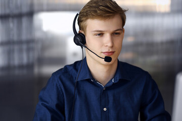 Young blond businessman using headset and computer at work. Startup business means working hard and out of time for success achievement