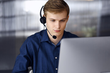 Young blond businessman using headset and computer at work. Startup business means working hard and...