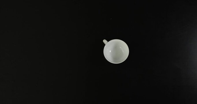 The above view of the white isolated clean empty cup spinning round at the black background. It stops in the end.