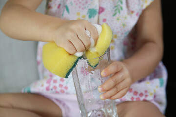 Child washing dishes in the kitchen. Cute two year old girl washes glass in sink. Early development, baby helps the parents. Chores for children.