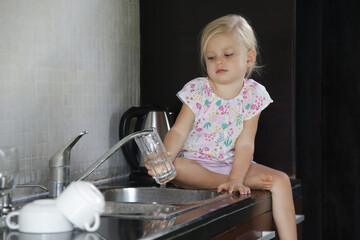 Child washing dishes in the kitchen. Cute two year old girl washes glass in sink. Early development, baby helps the parents. Chores for children.