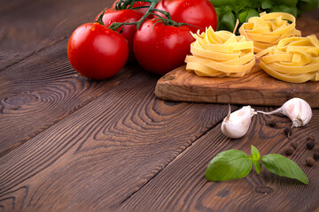 Raw tagliatelle pasta with fresh basil, garlic and branch of tomatoes on rustic wooden table