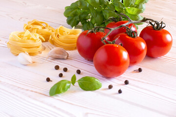 Raw tagliatelle pasta with fresh basil, garlic and tomatoes on a rustic white table, Copy space
