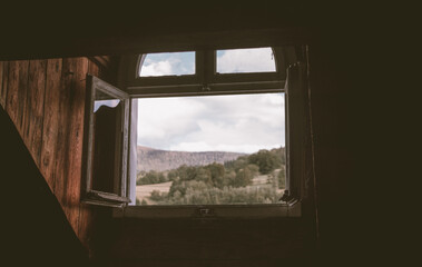Old windows open in the wood attic with a view of the forest in the mountains