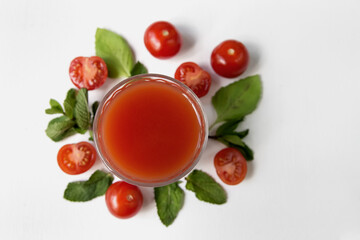  A glass with beautiful tomato juice on a background of tomatoes and greens, close-up.  Beautiful composition of a glass with tomato juice, podor, basil leaves and mint on a white background, minimali