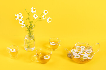 Three cups of camomile tea, transparent teapot and vase with daisy-like flowers on yellow background. Chamomile Tea Benefits Your Health concept