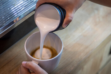 Barista in cafe or coffee bar preparing proper cappuccino pouring milk froth in a cup. Waiter hands pouring milk making cappuccino. barista pouring milk into coffee.