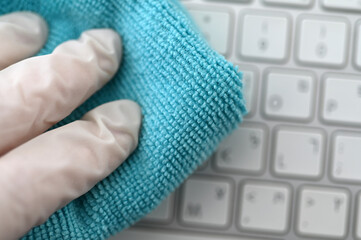 Hand with protective glove wiping a computer keyboard