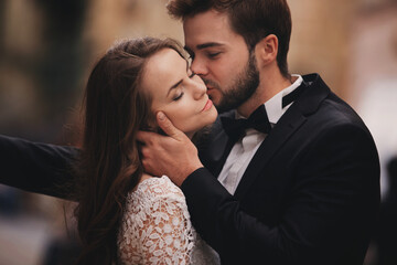 Happy newlywed couple hugging and kissing in old European town street, gorgeous bride in white wedding dress together with handsome groom. wedding day