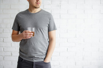 alcoholism concept - young man holding glass of whiskey over white brick wall  background