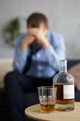 close up of whiskey bottle and glass and depressed businessman