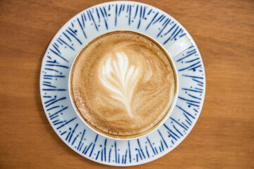 Cup of coffee latte with leaf design art in froth, on a wooden table and viewed from top