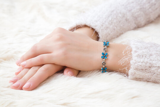 Flower bracelet on young woman hand wrist on white, fluffy fur blanket. Skin care and beauty in winter time. Closeup.