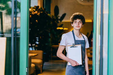 Young toughtful curly italian male waiter with food on tray serving at restaurant outdoor.Side jobs in bakery shop. Family business concept.