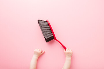 Baby hand holding red broom on light pink floor background. Regular cleanup in nursery room. Closeup. Point of view shot. Top down view.