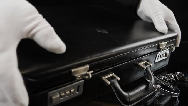 Mai in white gloves opens a briefcase full of gold bars. Handcuffed case with fine gold bars. Shiny gold bars in close-up view, 4K resolution