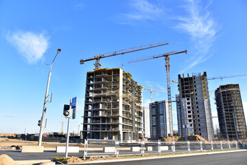 Fototapeta na wymiar Tower cranes working at construction site on blue sky background. Construction process of the new modern residential buildings. Tall house renovation project, government programs.