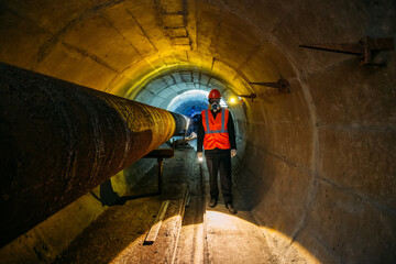 Tunnel worker examines pipeline in underground tunnel