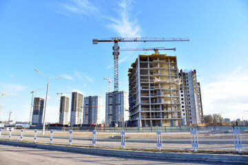 Tower cranes working at construction site on blue sky background. Construction process of the new modern residential buildings. Tall house renovation project, government programs.