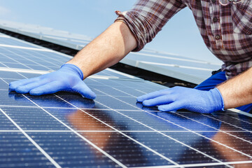Male worker hands in glows on solar panel, technician installing solar panels on roof. Alternative...